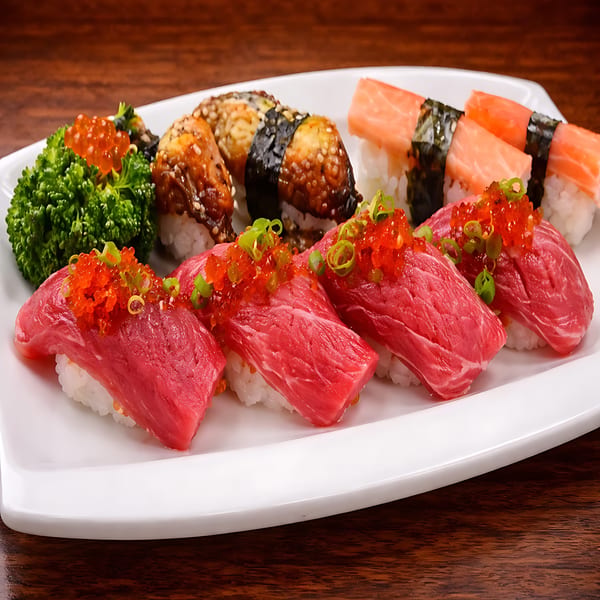 A white platter holds various sushi pieces, including tuna, salmon, and eel nigiri, with green garnish.