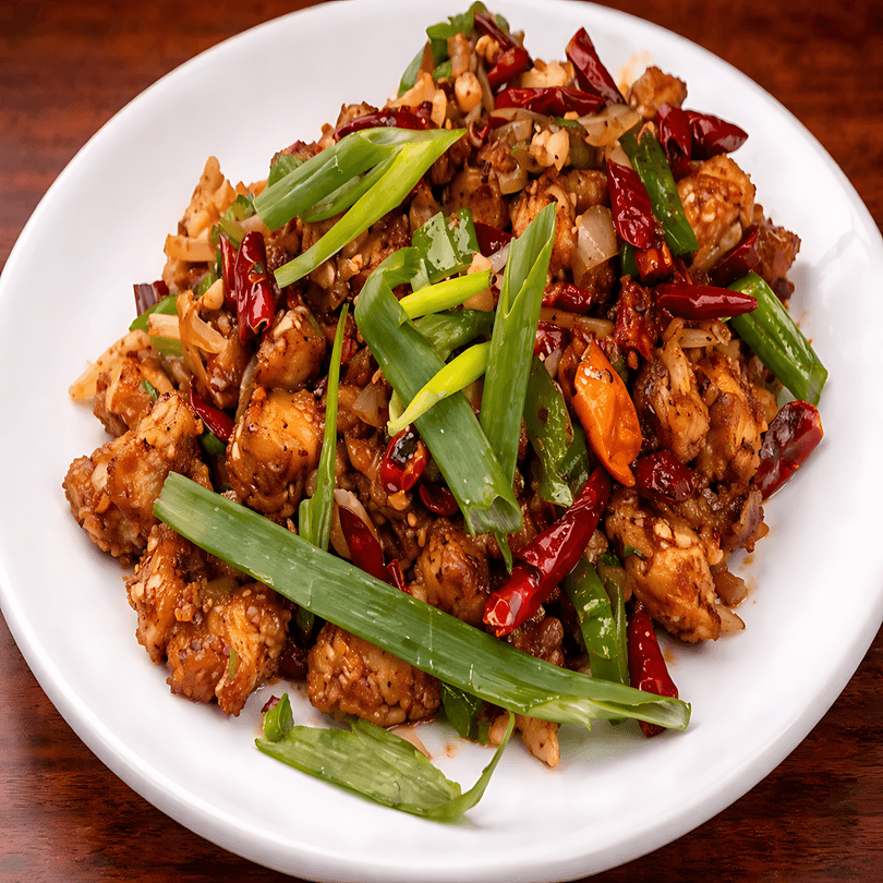Spicy Kung Pao chicken with peanuts, red chili peppers, and green onions on a white plate.