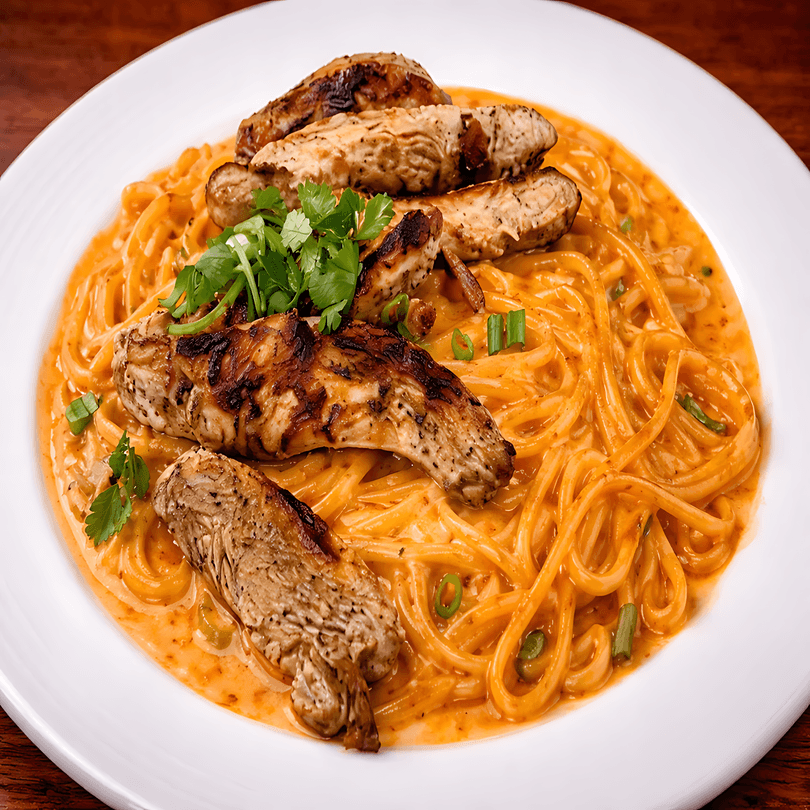 Grilled chicken strips over spaghetti in a creamy orange sauce, garnished with fresh cilantro and green onions.